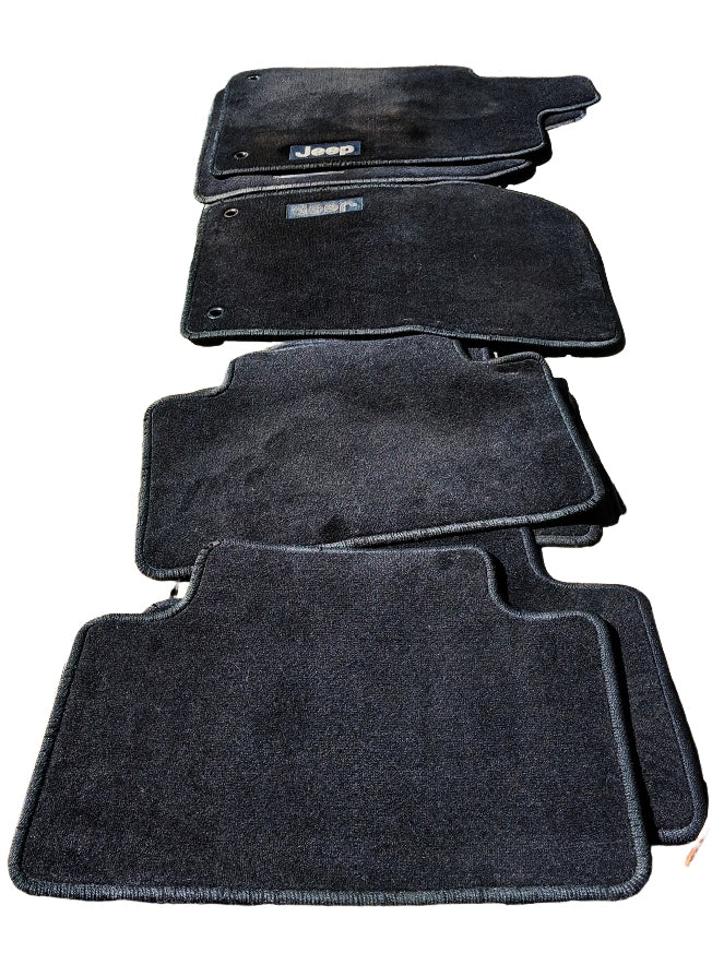 A set of black WK2 Grand Cherokee Floor mats Front and Rear  mats show the Jeep logo, indicating the brand is original Genuine Jeep.