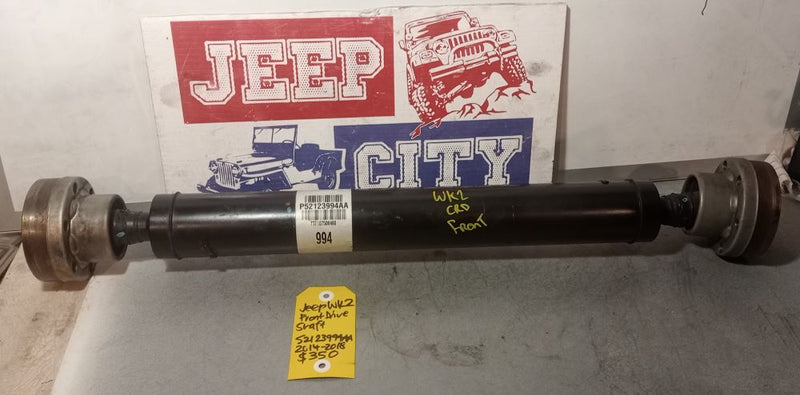 A pre-owned Jeep WK2 Grand Cherokee drive shaft displayed on a table with a Jeep City onlinebranded backdrop.