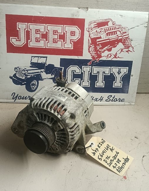 A used automotive alternator with a handwritten price tag, displayed in front of a 'Jeep City' sign on a worn white surface.