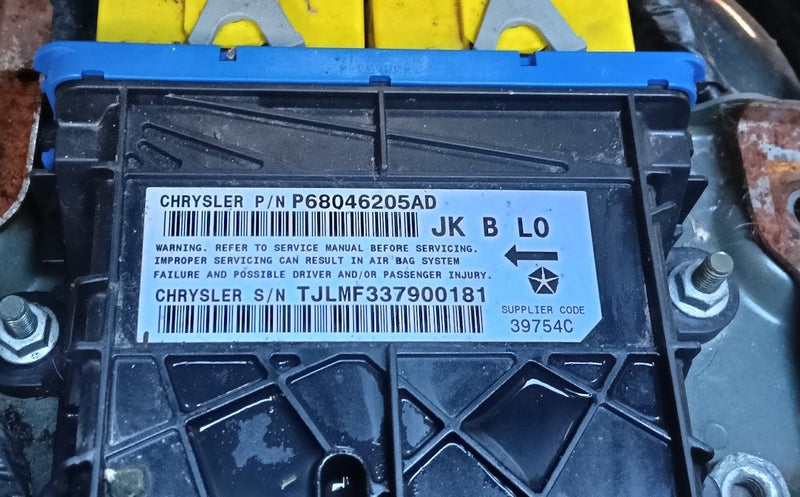 A close-up of a black plastic automotive part with a blue top section and a white printed label. The label reads Chrysler with part number P68046205AD and other part details.