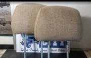 Two beige woven fabric headrests for a vehicle, displayed on metal stands in front of a store sign.