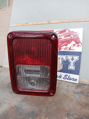 A red tail light for a Jeep JK Wrangler, featuring the light, bulbs, and wire harness, displayed against a sign.
