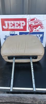 A beige leather Jeep seat cushion Headrest with metal support arms, shown against a background featuring a Jeep logo sign.