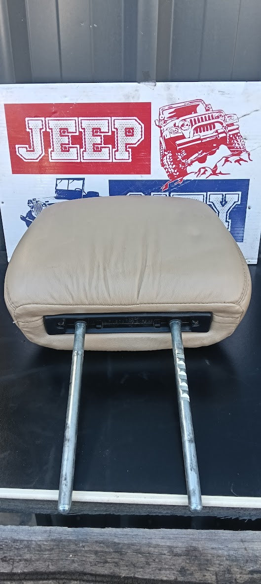 A beige leather Jeep seat cushion Headrest with metal support arms, shown against a background featuring a Jeep logo sign.