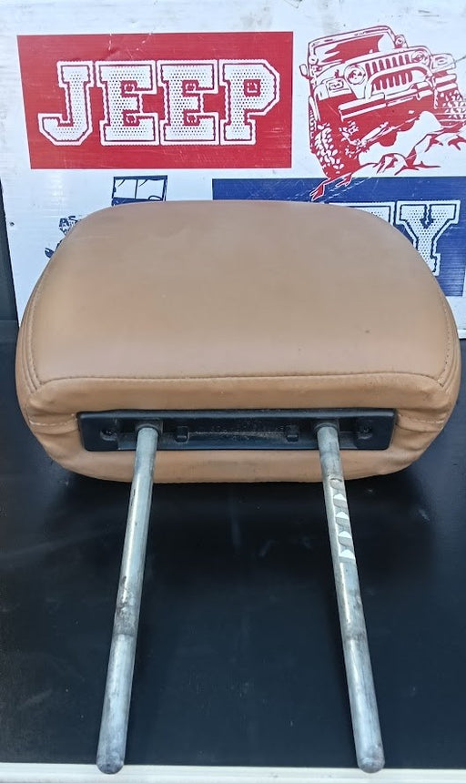 A tan leather car center console armrest with two metal mounting posts, shown against a background featuring a red and white Jeep logo.