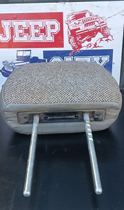 A used beige woven fabric headrest pillow with two metal mounting pins, shown against a background featuring a vintage red and white Jeep sign.