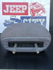 A used gray fabric car headrest or seat cushion with two metal support rods, shown against a background featuring a 'Jeep City' sign.