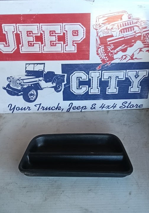 A black plastic rectangular tray or organizer insert placed on a light-colored wooden surface, with a printed sign in the background featuring Jeep and truck graphics and the text 'Your Truck, Jeep & 4x4 Store'.