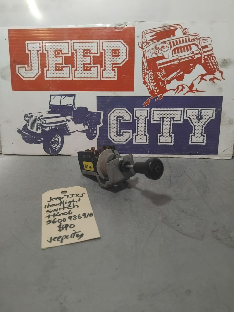 A Jeep TJ XJ headlight switch with knob, positioned in front of a 'Jeep City' themed sign.
